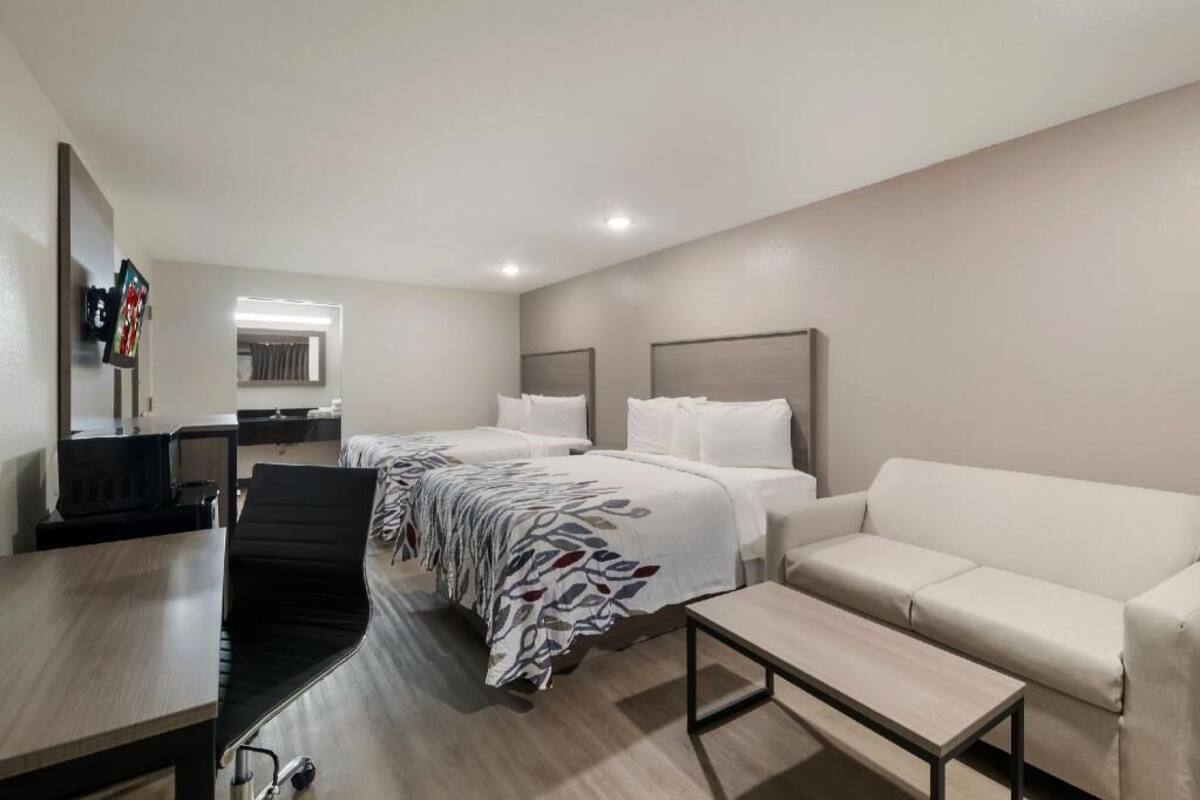 A hotel room with two beds, a sofa, a desk, and a chair.