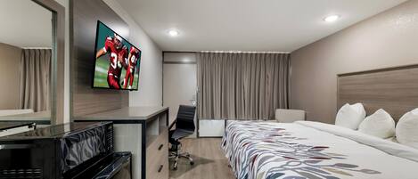 Una habitación de hotel con cama, escritorio con microondas, televisión y una silla.