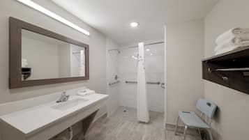 A modern bathroom with a large mirror, two sinks, a shower with a glass door, and a towel rack.