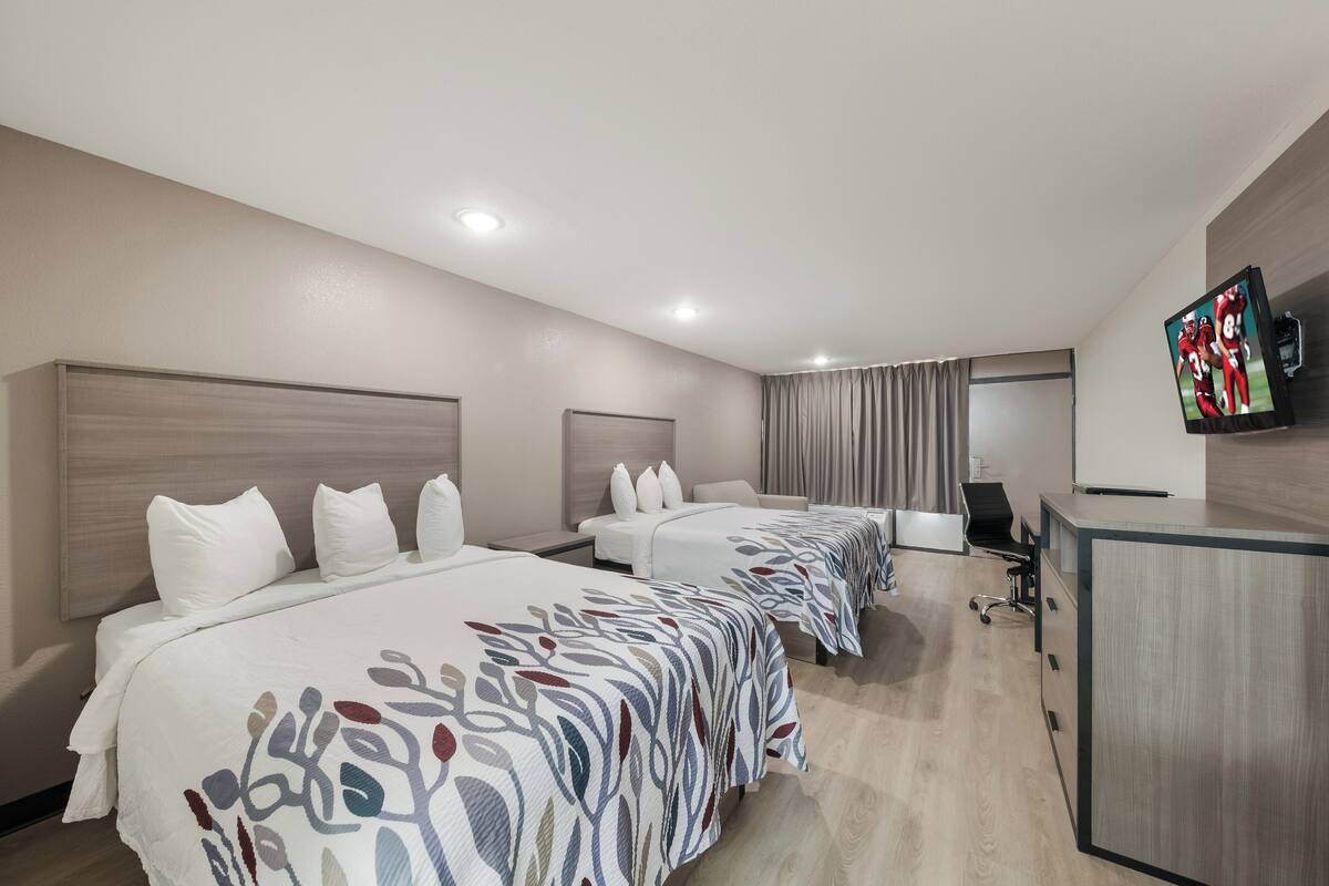 A hotel room with three beds, a desk, a television, and a wardrobe.