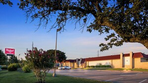 A Red Roof Inn with a parking lot, a building with a red roof, and a clear sky.