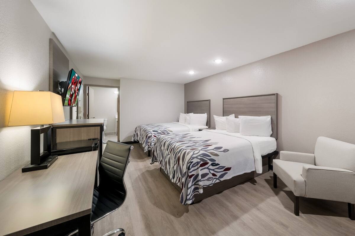 A hotel room with two beds, a desk, a chair, and a TV.