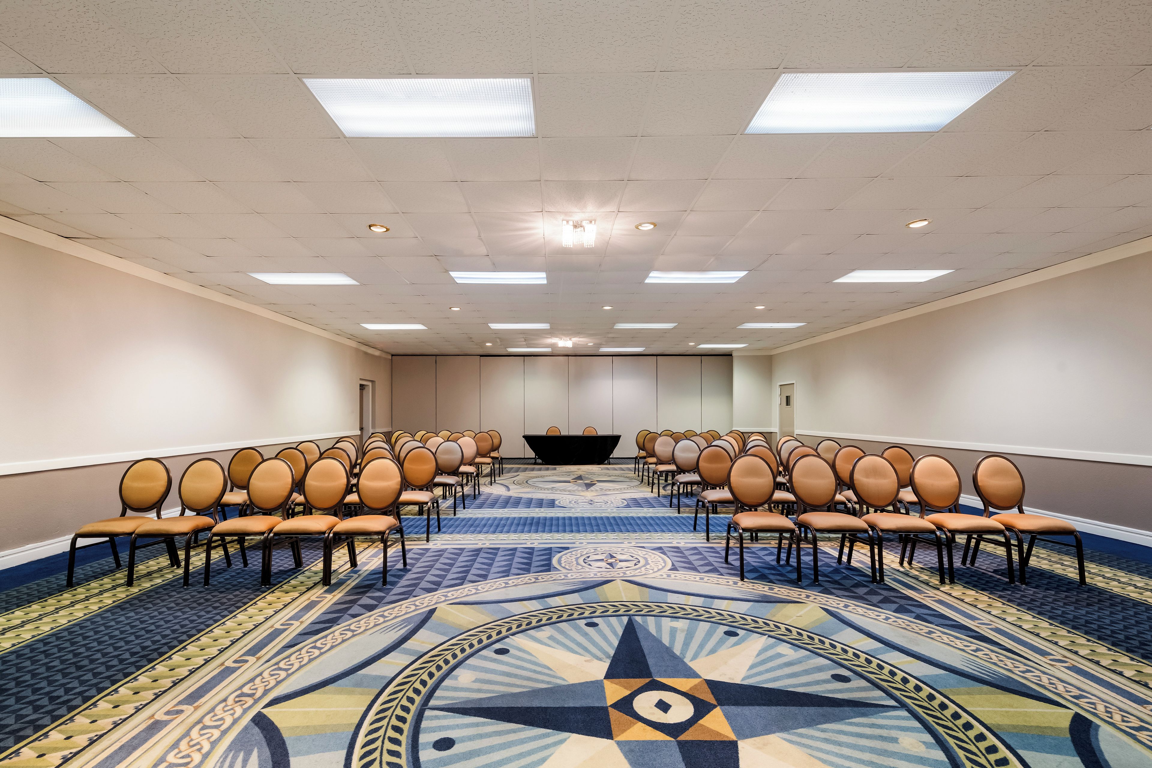 Un salón de conferencias con filas de sillas, un escenario y una alfombra estampada.