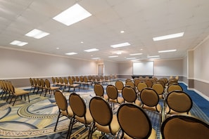 Un salón de conferencias con filas de sillas, un escenario y suelo alfombrado.