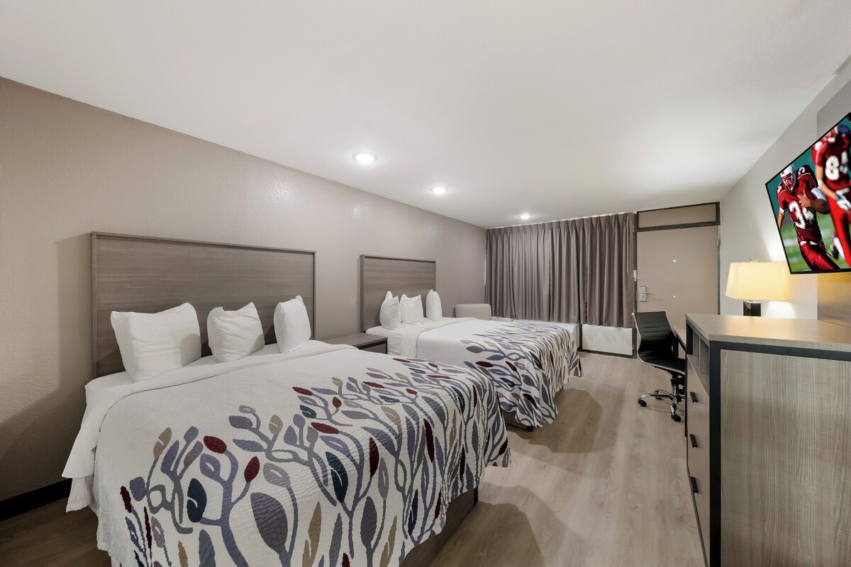 A hotel room with two beds, a desk, a TV, and a curtain.