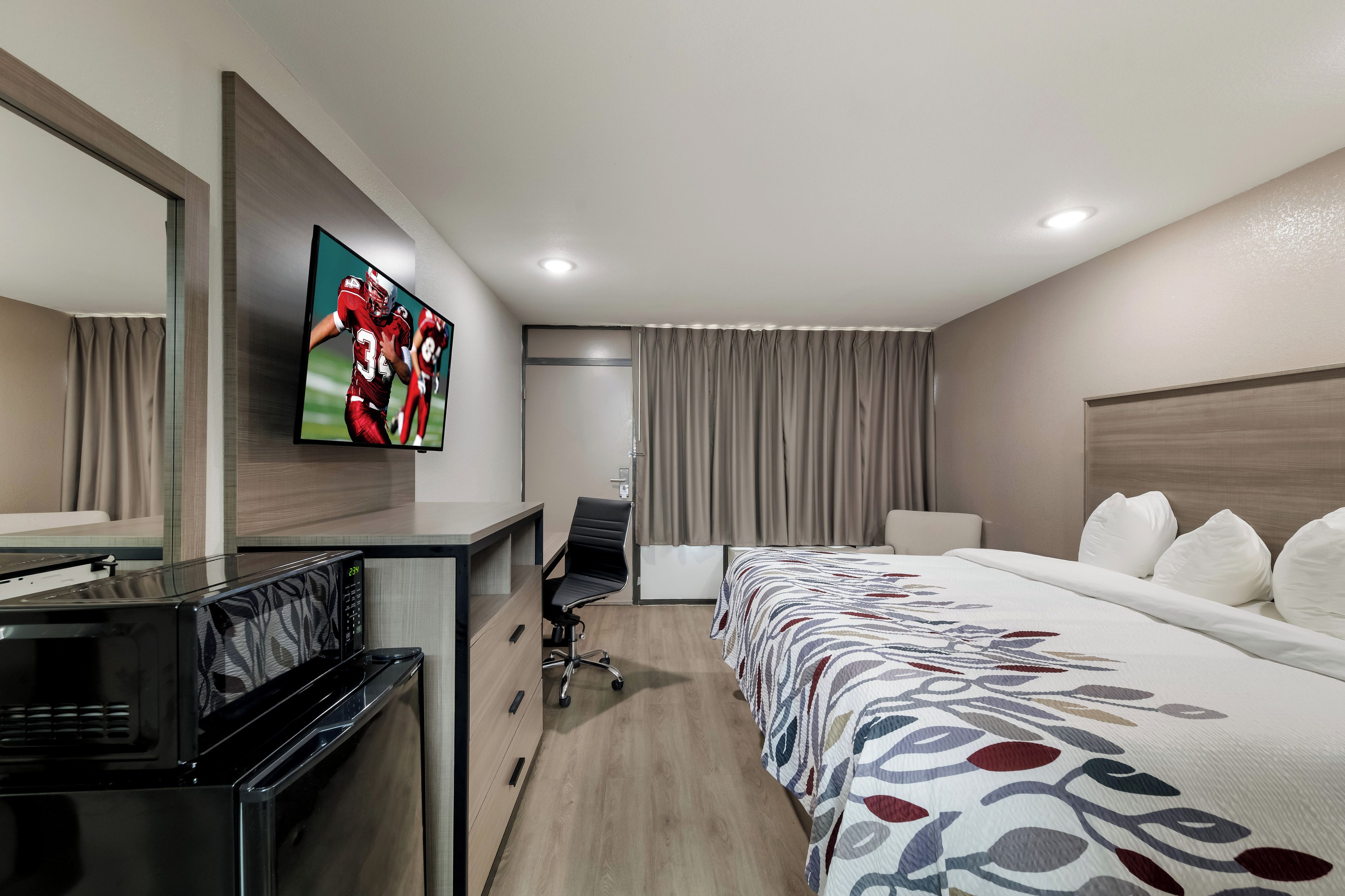Una habitación de hotel con cama, escritorio, silla, televisor y microondas.