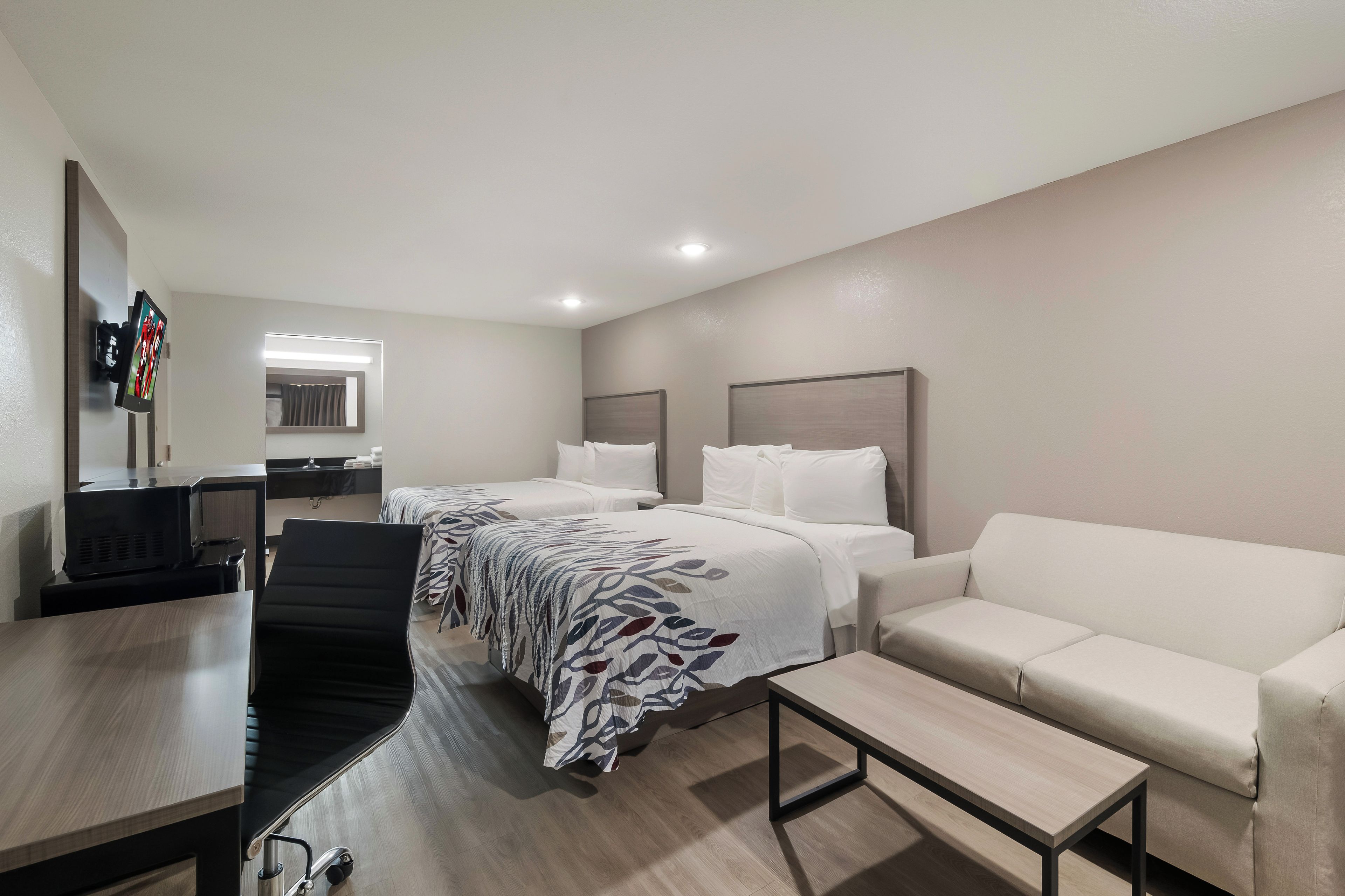 A hotel room with two beds, a sofa, a desk, and a TV.