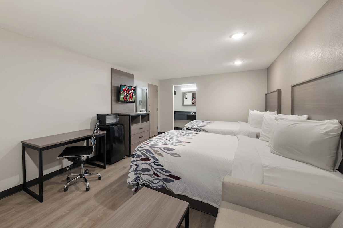 A hotel room with a desk, two beds, a chair, and a TV.