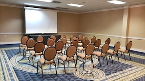 A conference room with rows of chairs, a projector screen, and patterned carpet. - Red Roof Inn & Conference Center McKinney (McKinney)