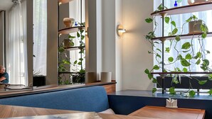 A modern interior with a wooden table, blue seating, and shelves with plants and books. - Hotel le Friedland (Paris)