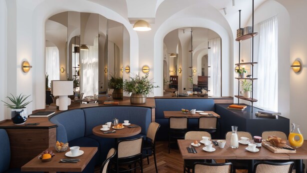 A modern dining area with round tables, blue upholstered seating, and a variety of breakfast items. - Hotel le Friedland (Paris)
