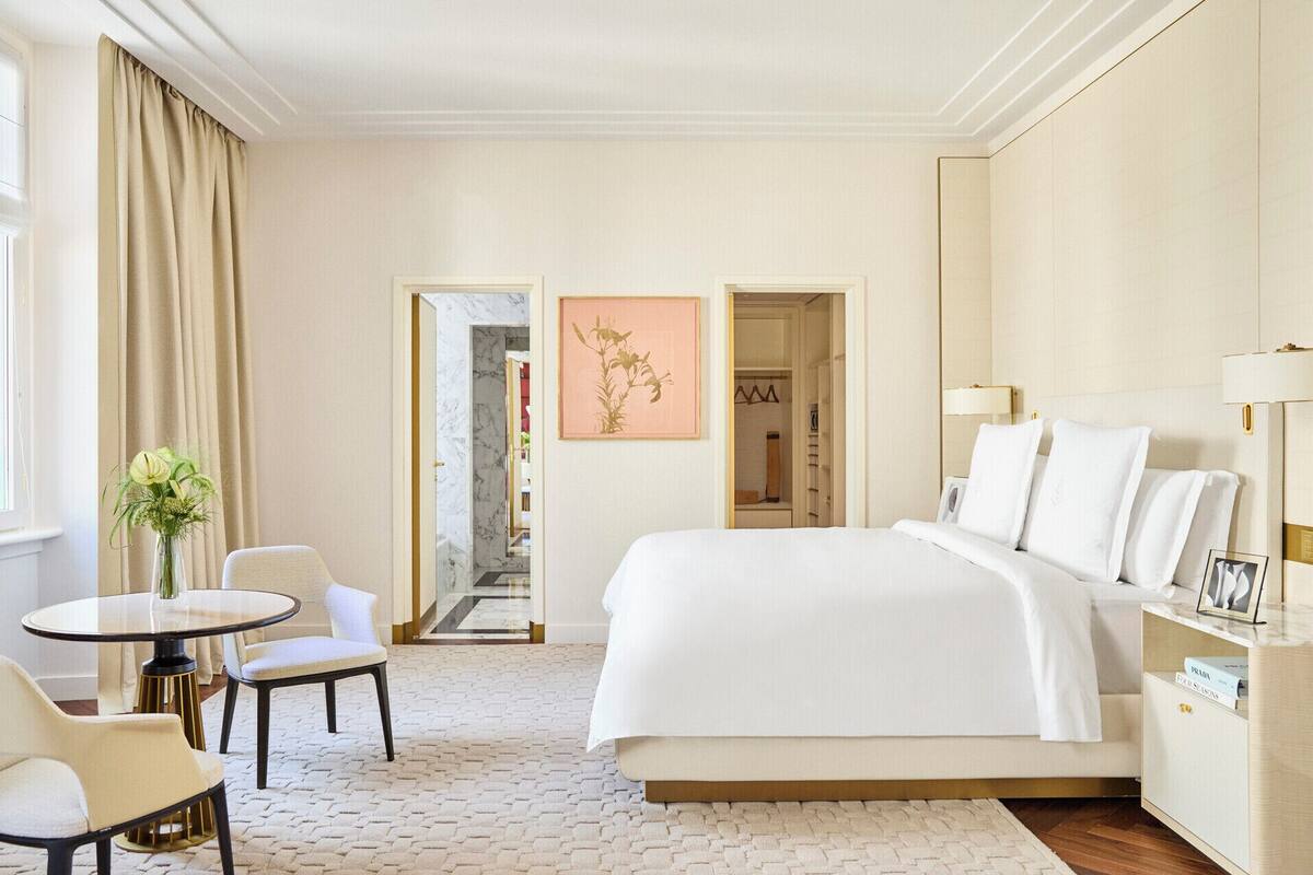 A hotel room with a large bed, a desk, a chair, a small table, and a vase with flowers.