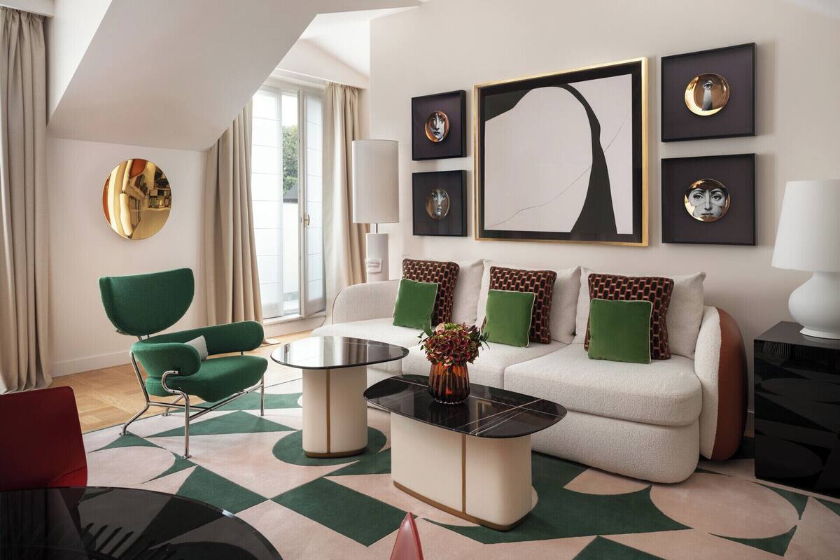 A modern living room with a green armchair, a white sofa with patterned cushions, a coffee table, and artwork on the walls.
