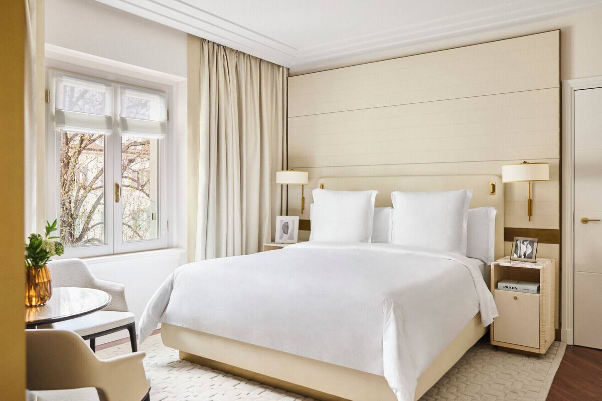A hotel room with a large bed, bedside tables, a desk with a chair, and a window with curtains.