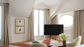 A modern hotel room with a large window, a flat-screen TV, a round window, and a vase with flowers.