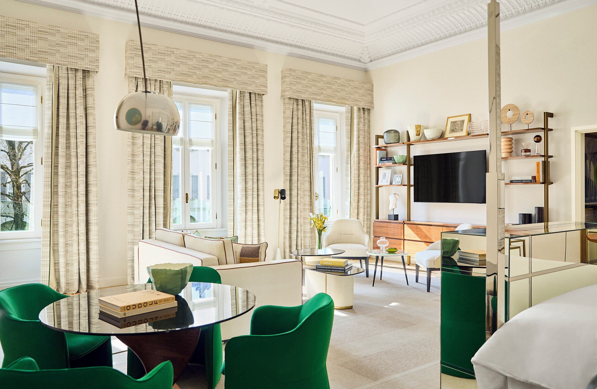 A modern living room with a glass coffee table, green chairs, a sofa, and a flat-screen TV.