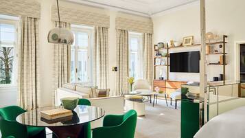 A modern living room with a glass coffee table, green chairs, a sofa, and a flat-screen TV.