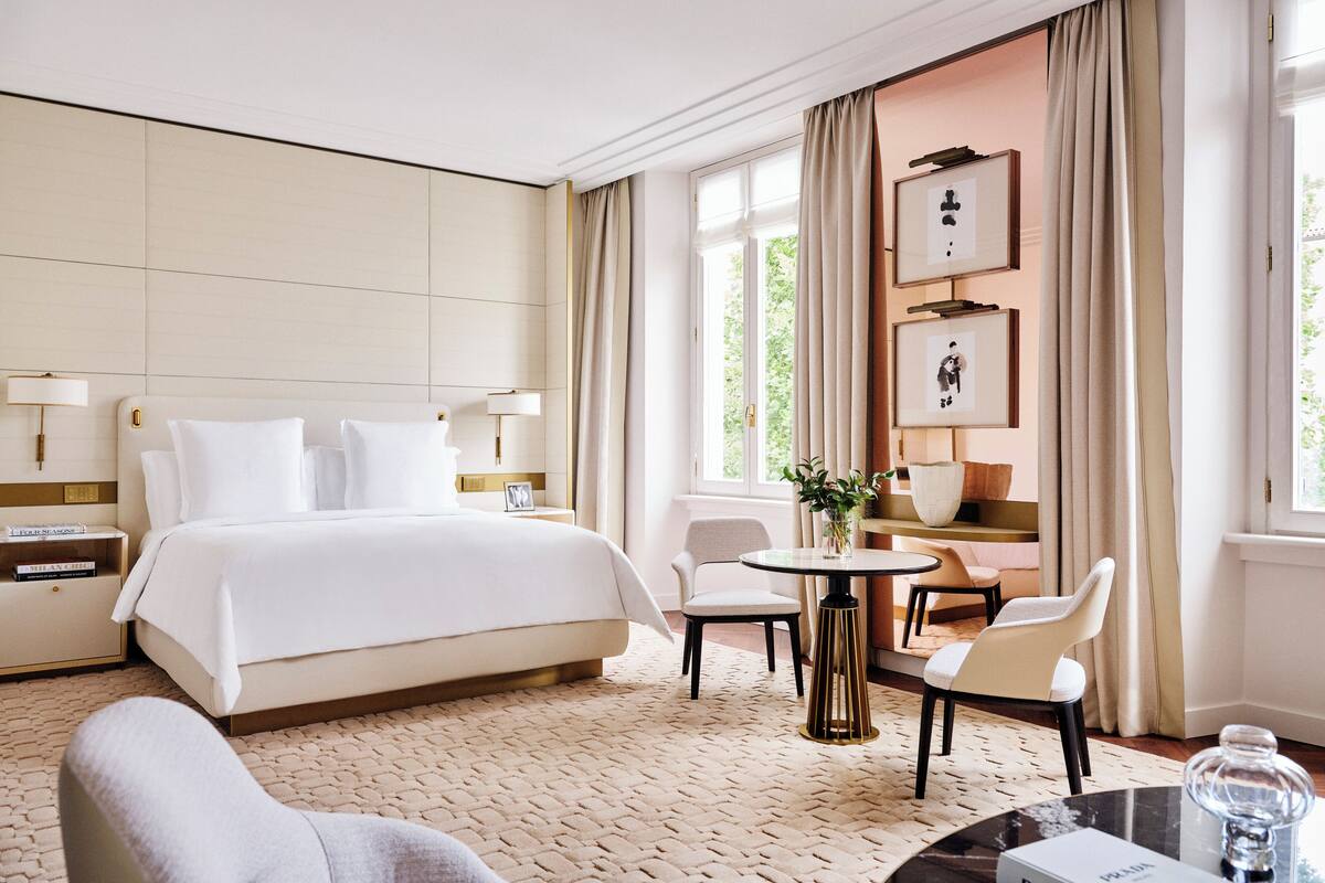 A hotel room with a large bed, a round table, two chairs, a nightstand, and a lamp.