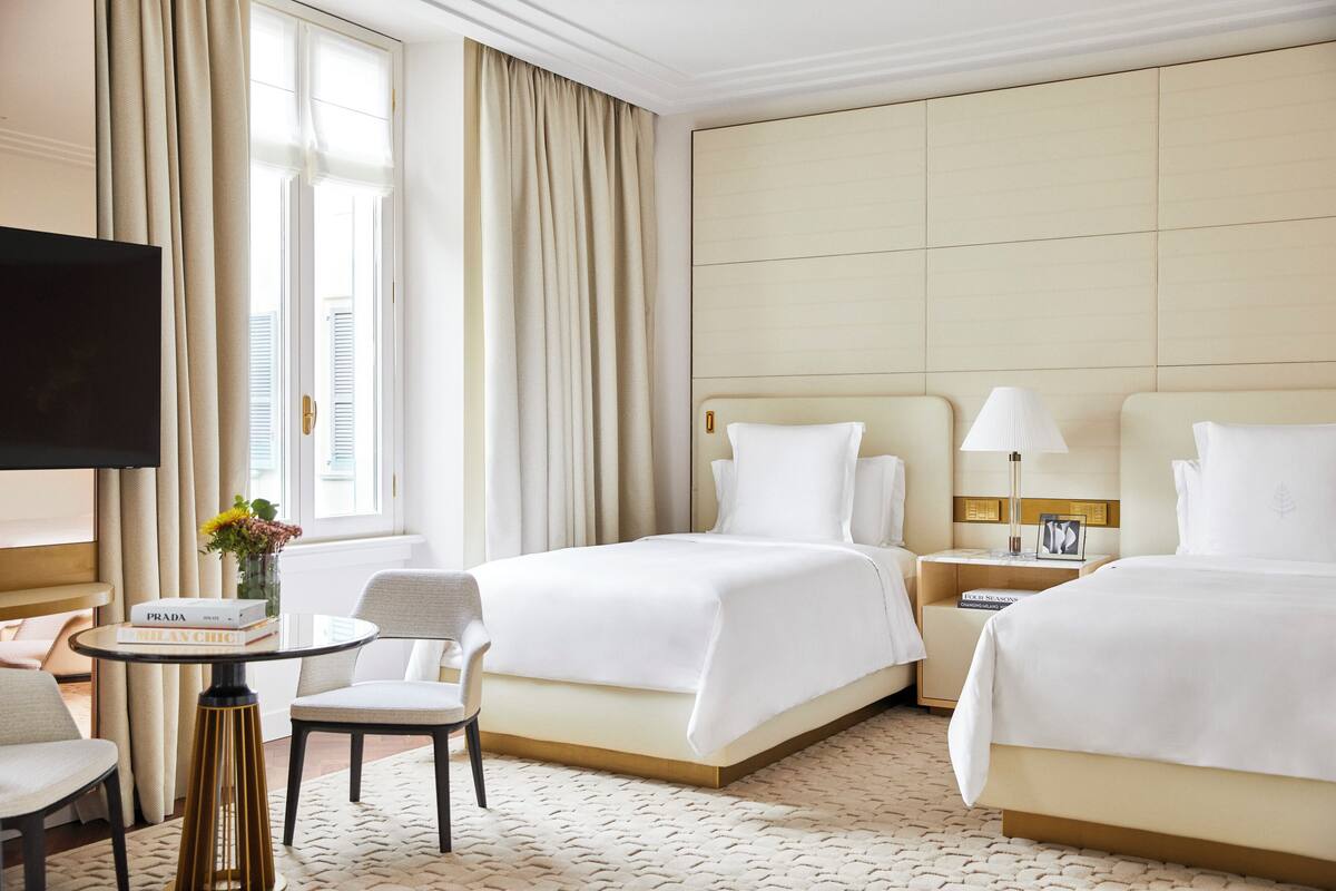 A hotel room with two beds, a TV, a small table with books, and a chair.