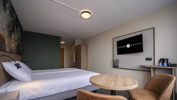 Habitación de hotel con cama, una mesa redonda, dos sillas, televisión en la pared y un cuadro.