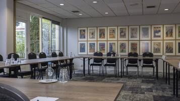Een vergaderzaal met een lange tafel, stoelen en kunstwerken in lijsten aan de muren.