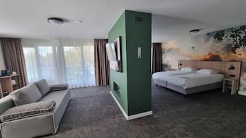 Ein Hotelzimmer mit einer Couch, einem Bett, einem Fernseher, einem Gemälde und einem Schreibtisch.