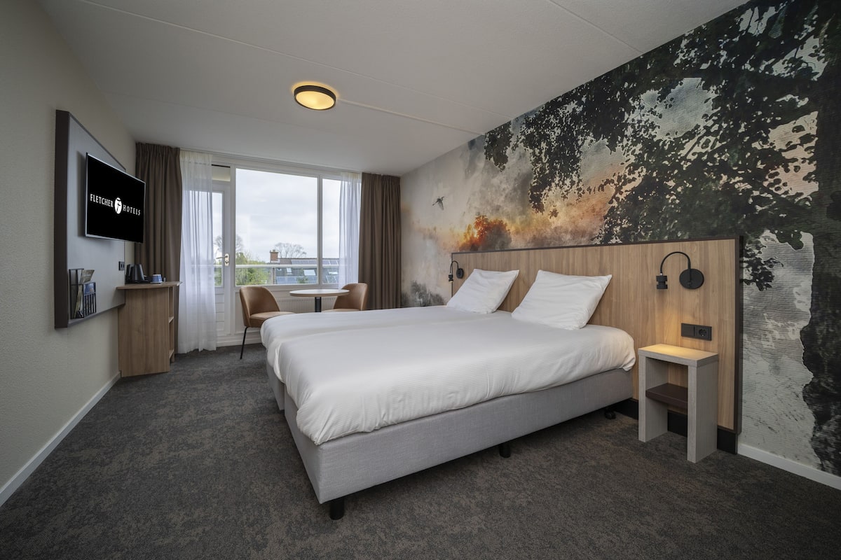 A hotel room with a large bed, a desk, a chair, a TV, and a mural on the wall.