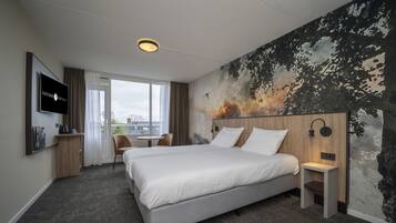 A hotel room with a large bed, a desk, a chair, a TV, and a mural on the wall.