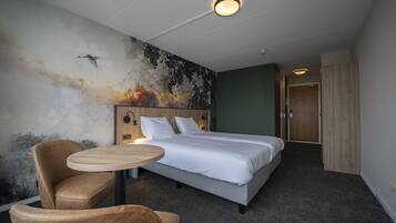 A hotel room with a bed, a round table, a chair, and a wall mural.