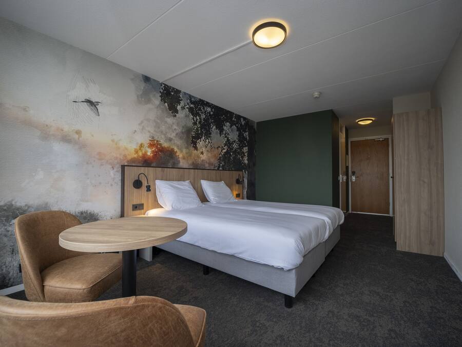 A hotel room with a bed, a round table, a chair, and a wall mural.