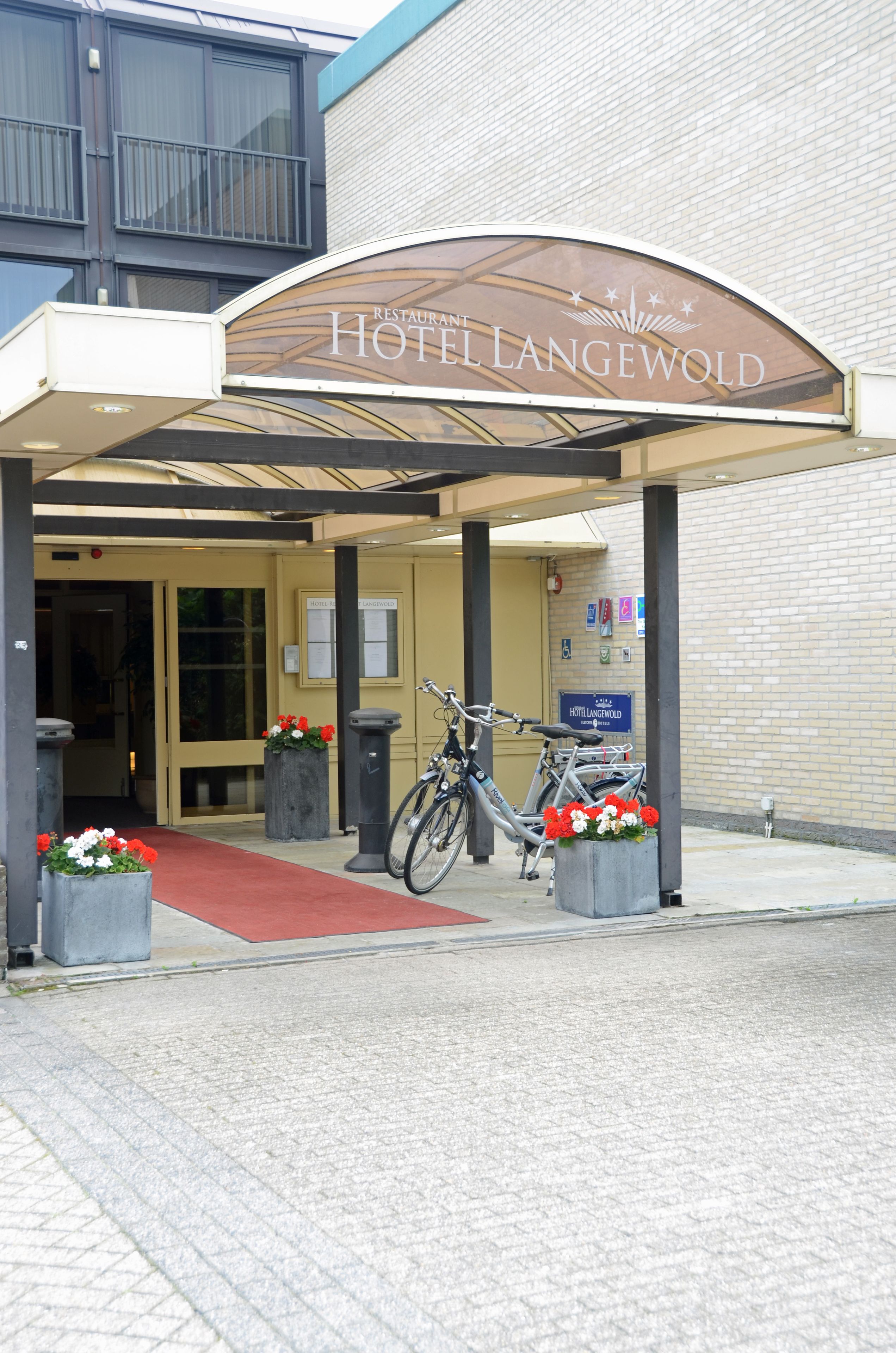 The entrance of the Hotel Langewold with a covered entrance, a red carpet, and bicycles parked outside.