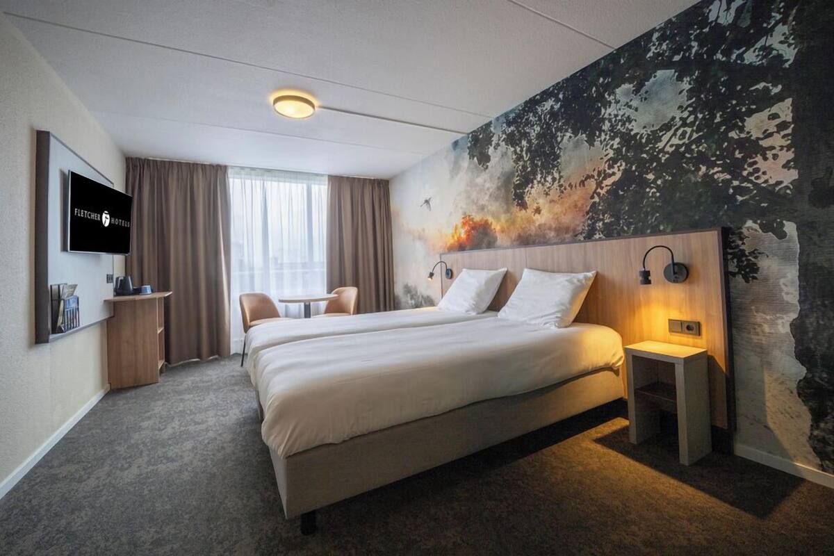 A hotel room with a large bed, a TV, a desk, and a mural on the wall.