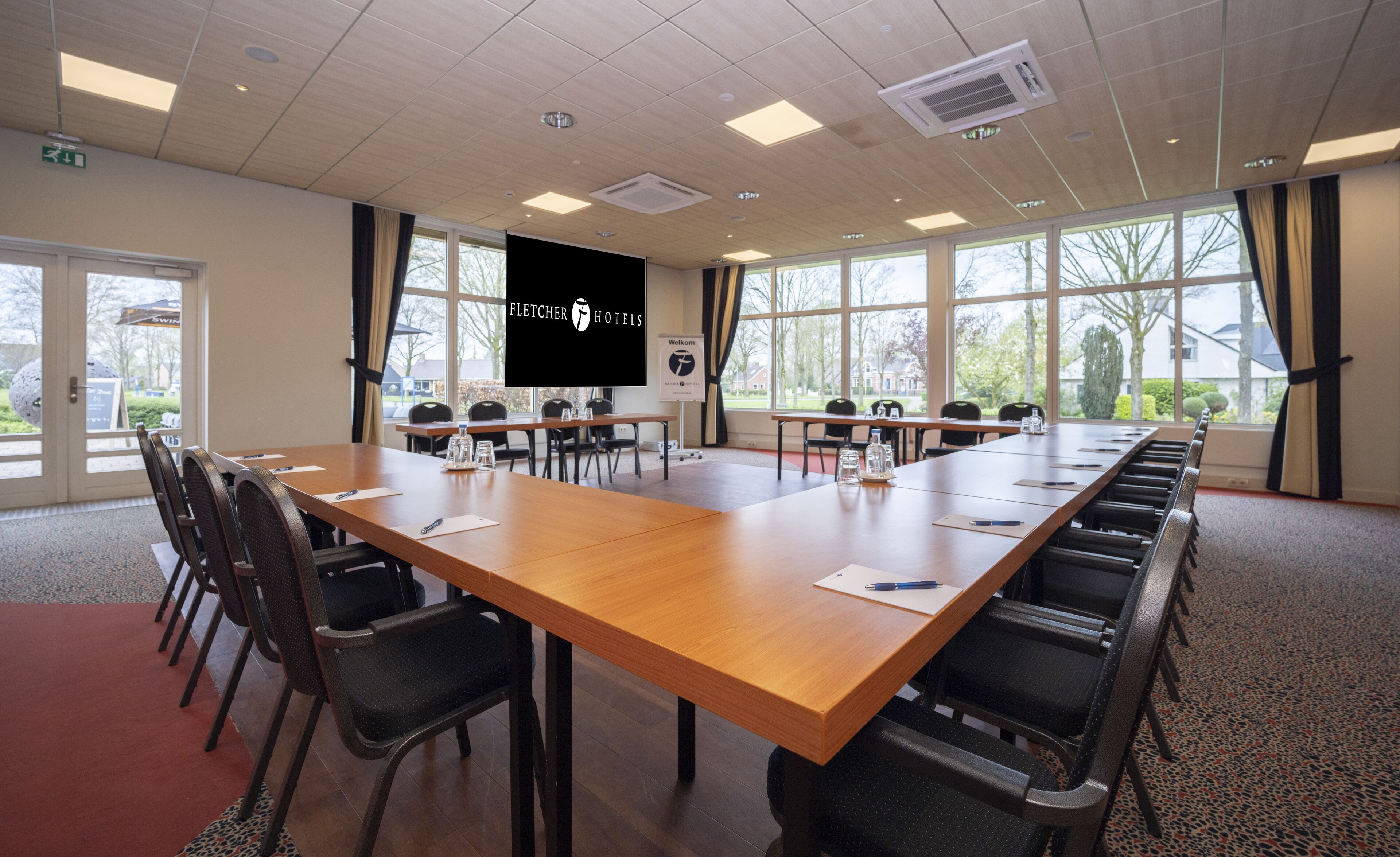 A conference room with a long wooden table, black chairs, and large windows.