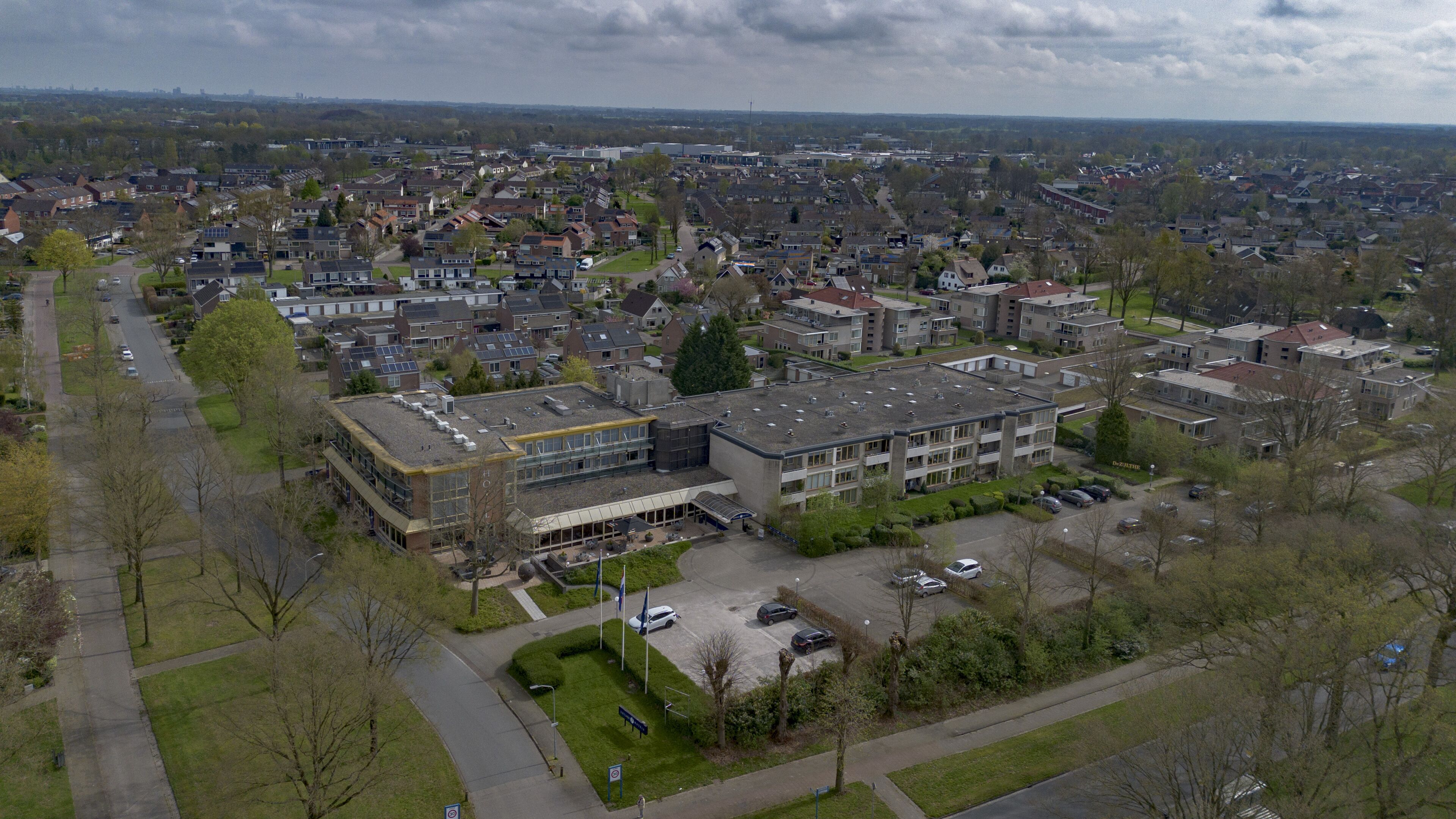 An aerial view of a residential area with a large building that appears to be a school or community center, surrounded by houses and streets.