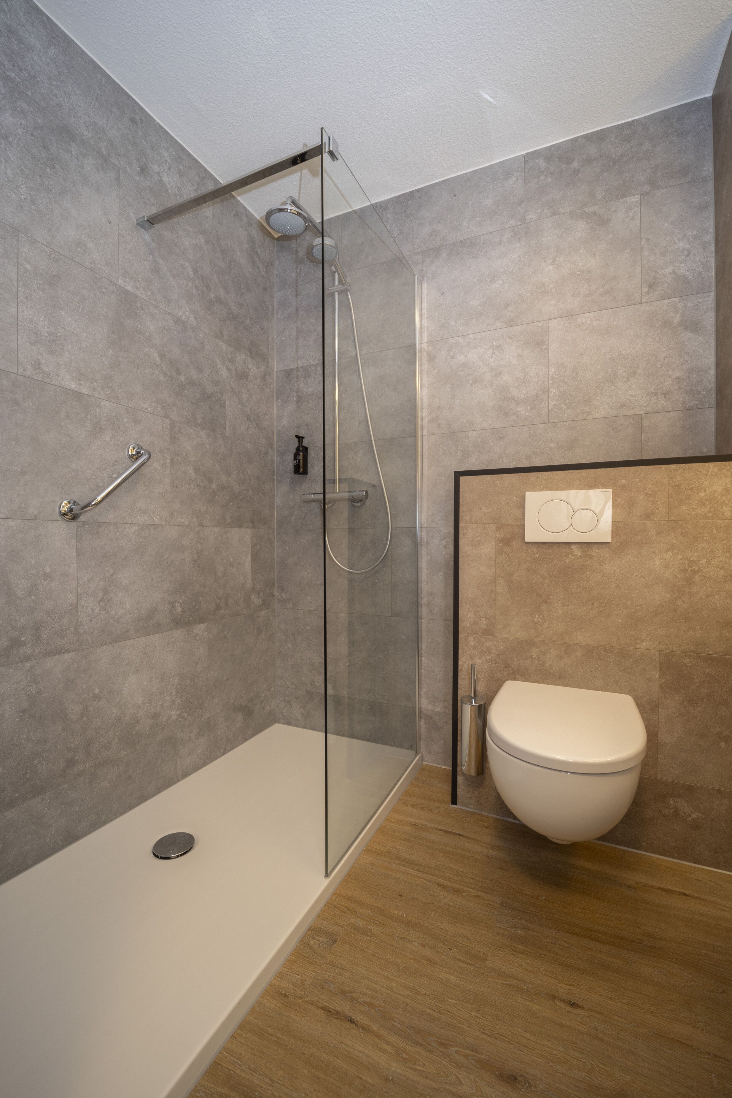 A modern bathroom with a glass-enclosed shower, a white toilet, and a wooden floor.