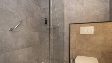 A modern bathroom with a glass-enclosed shower, a white toilet, and a wooden floor.