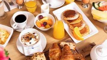 Ein Frühstückstisch mit Croissants, Pfannkuchen, Obst, Kaffee und Saft.