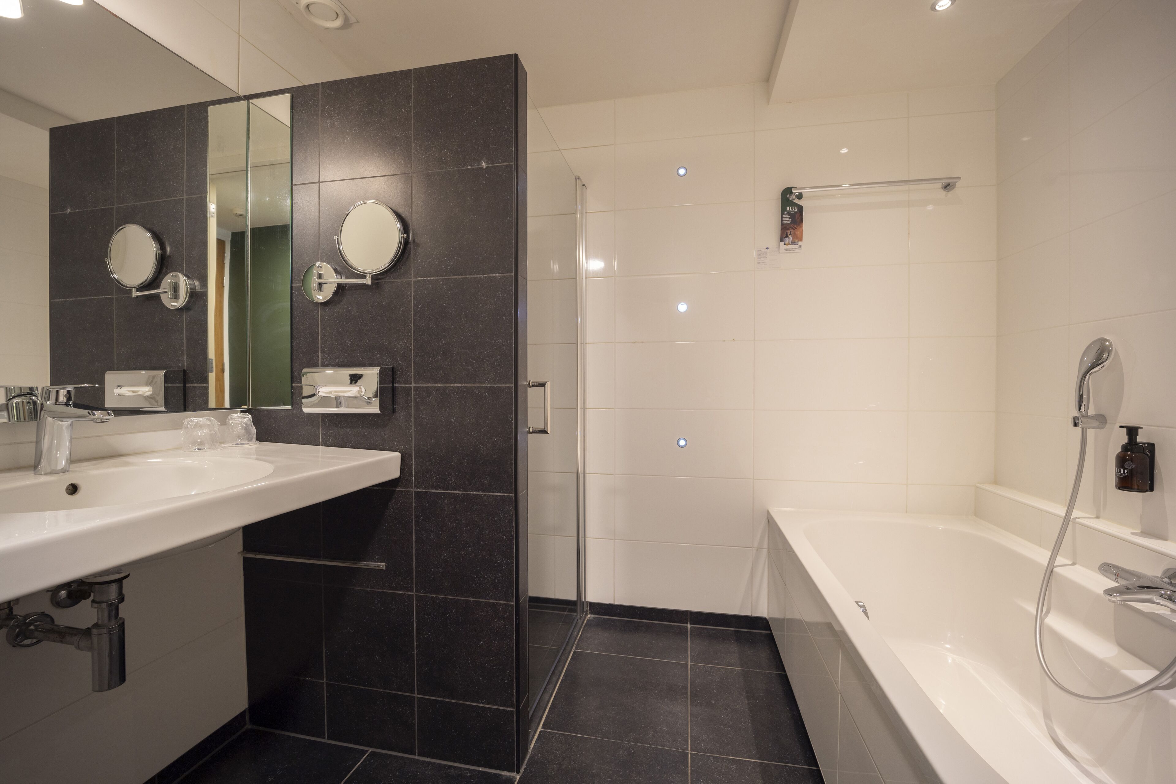 A modern bathroom with a large mirror, two sinks, a shower, and a bathtub.