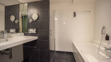 A modern bathroom with a large mirror, two sinks, a shower, and a bathtub.