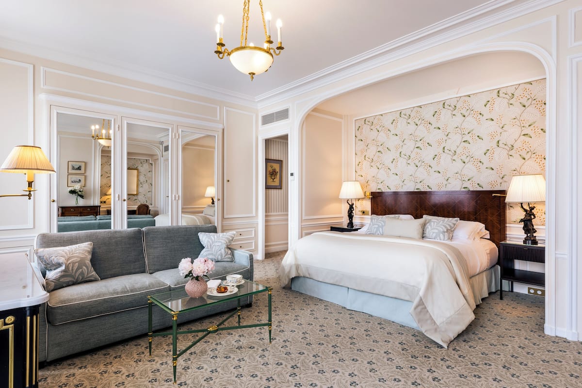 Una habitación de hotel con una cama grande, un sofá, una mesa de centro de vidrio y una araña.