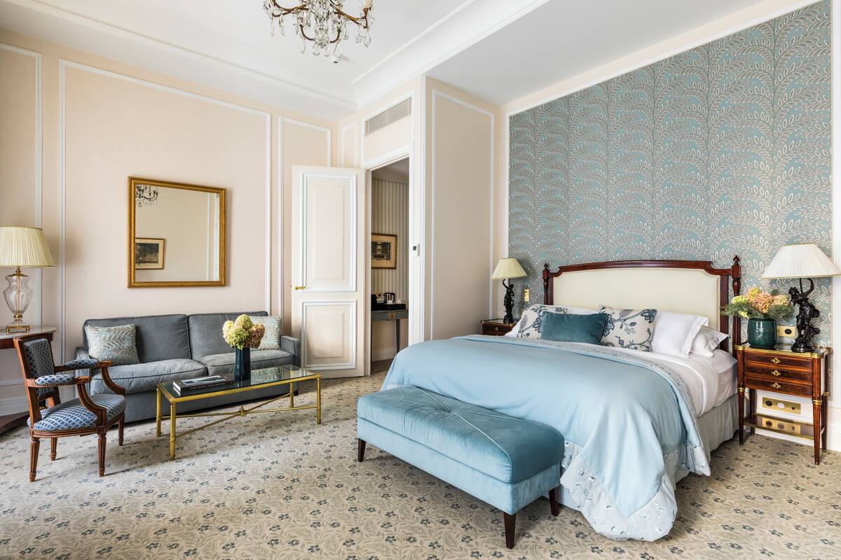 Un dormitorio con una cama grande, un sofá, una mesa de centro y una silla. Hay una puerta que da a otra habitación.