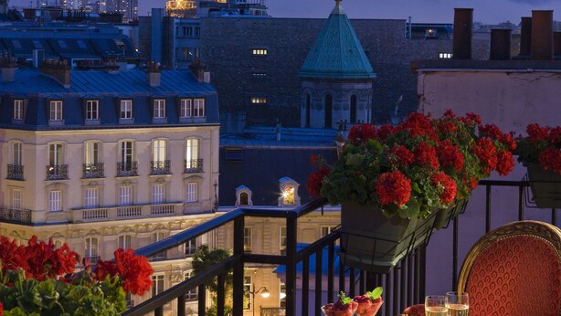 A terrace with a view of the Eiffel Tower, a table with drinks, and red flowers. - Hôtel San Régis (Paris)