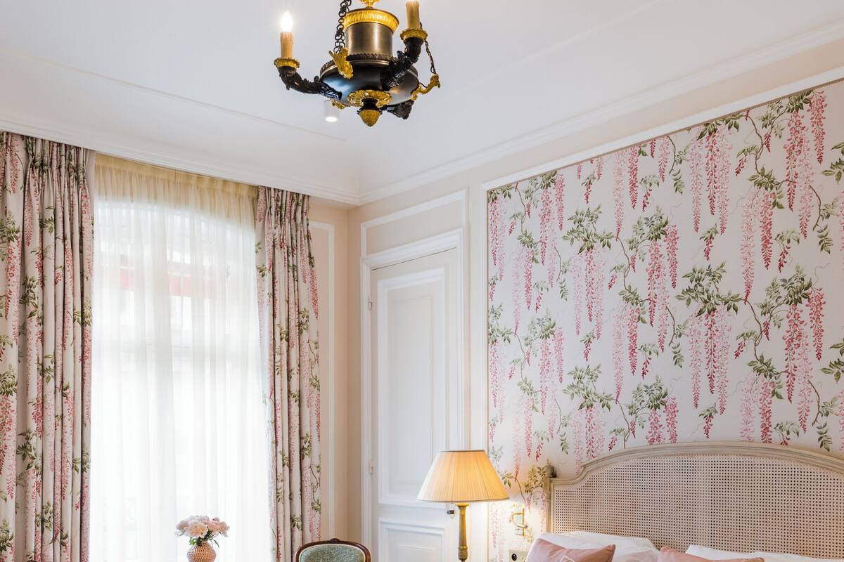 Un dormitorio con una cama grande, dos sillas, una mesita, una lámpara y un candelabro.
