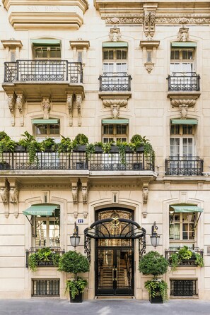 A multi-story building with balconies, ornate iron railings, and green awnings.