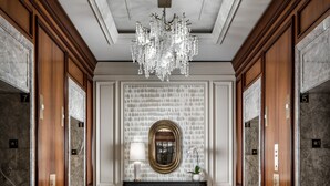 A luxurious lobby with marble flooring, a grand chandelier, and a central console with a gold emblem.