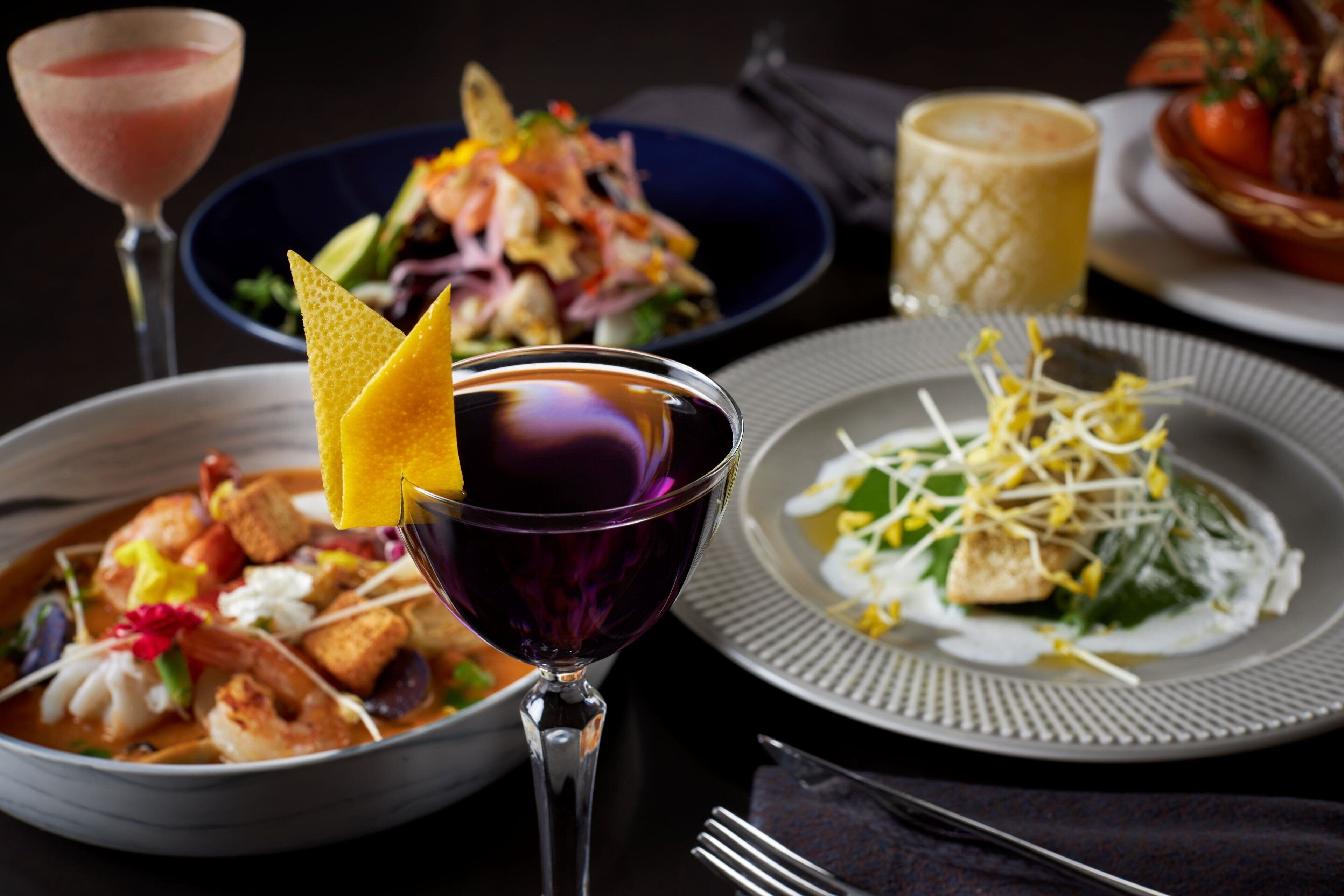 A table set with various dishes, including a bowl of soup, a plate with a salad, and a glass of a purple-colored drink.
