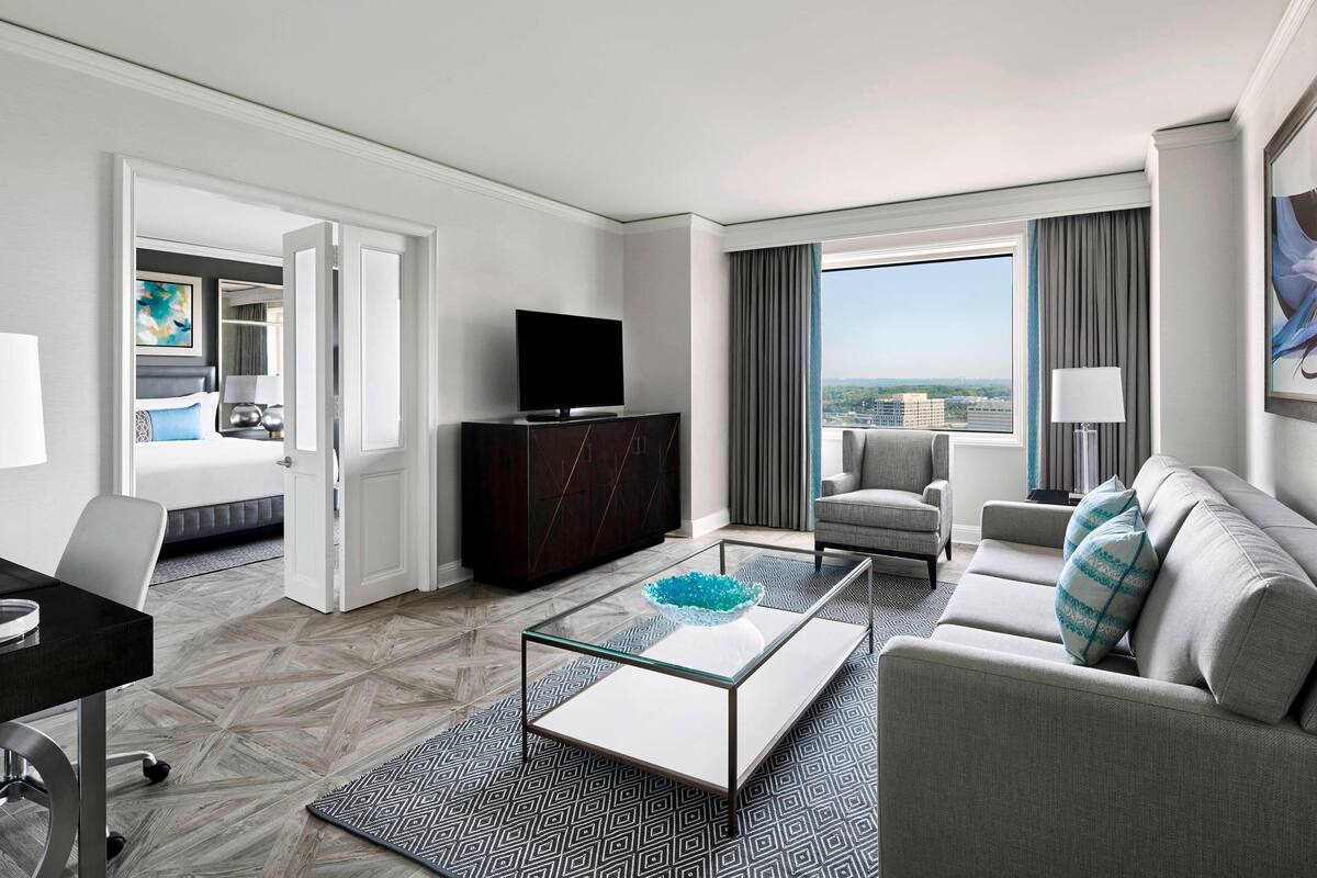 Une chambre d’hôtel au design moderne, comprenant un canapé, une table basse en verre, un téléviseur à écran plat et une vue sur la ville.