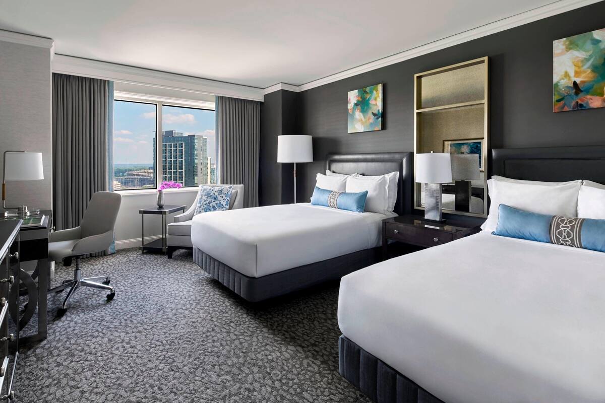 Une chambre d’hôtel avec deux lits, un bureau, une chaise, une lampe et une vue sur la ville.