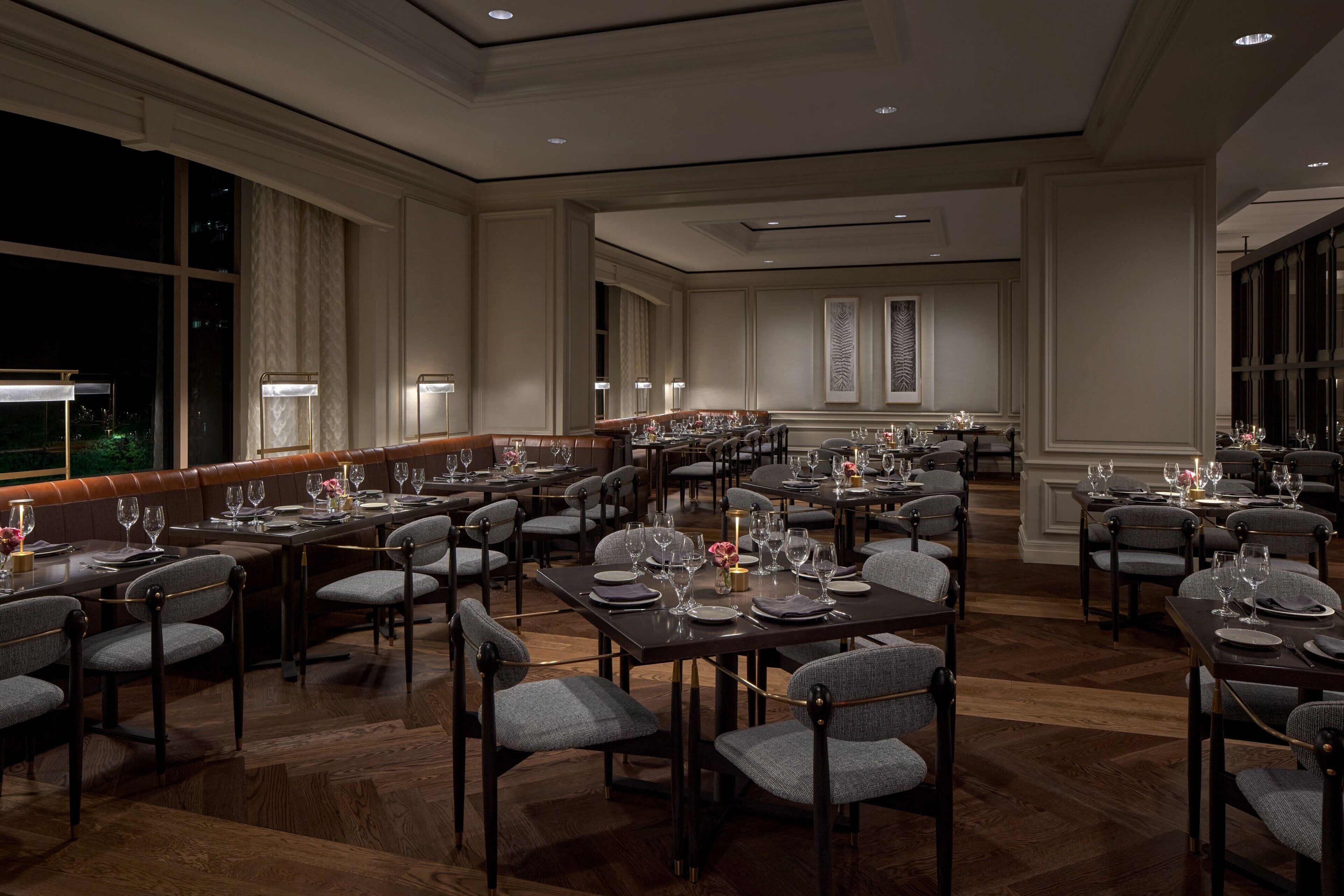 Un comedor amplio con varias mesas y sillas, iluminación elegante y vistas al exterior.