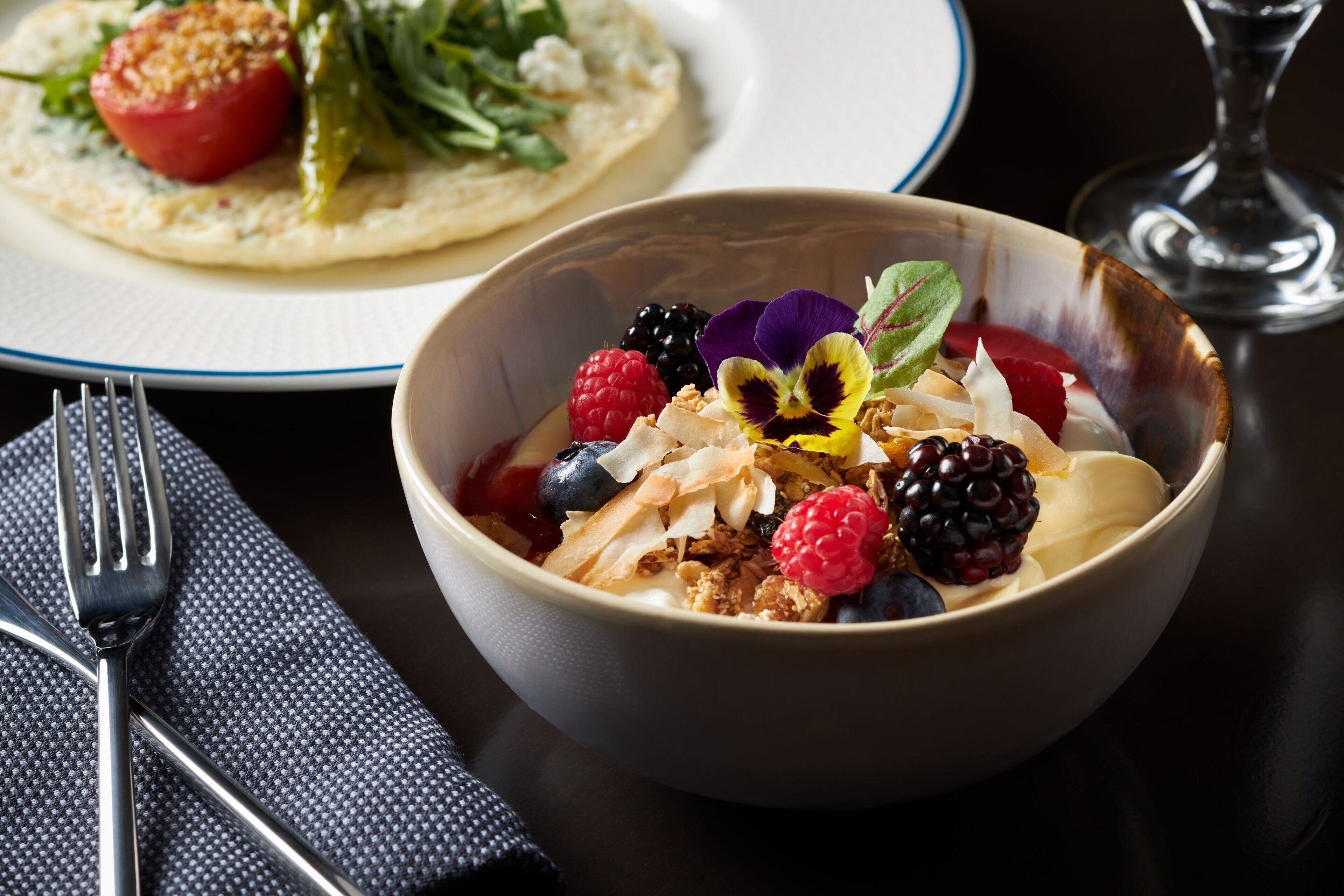 A bowl of fruit salad with various berries and a glass of water on a table.